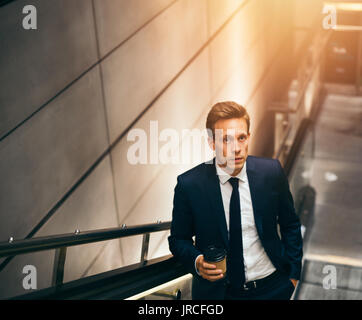 Junge Geschäftsmann im Anzug trinken einen Kaffee und Reiten auf einer Rolltreppe in der U-Bahn während der morgendlichen Fahrt zum Arbeitsplatz Stockfoto