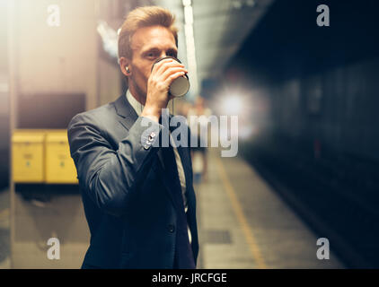 Junge Unternehmer bei Kaffee und Musik auf sein Handy beim Stehen auf einer u-Plattform während seines morgendlichen Fahrt Stockfoto