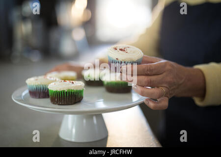 Den mittleren Abschnitt der älteren Frau Aufnehmen der Cupcake aus dem Fach Stockfoto