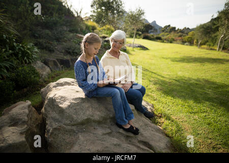 Lächelnd Enkelin und Oma lesen Buchen Sie im Garten an einem sonnigen Tag Stockfoto