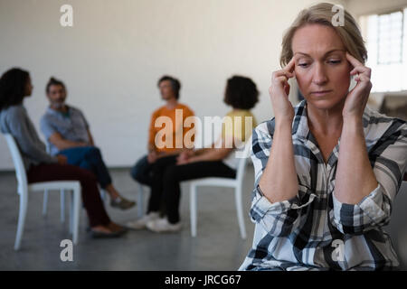 Verspannte Frau mit Kopf in der Hand, während Freunde diskutieren im Hintergrund bei Kunst Klasse Stockfoto