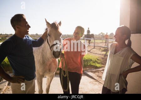 Trainer im Gespräch mit Frauen beim Stehen auf dem Pferd im Stall Stockfoto