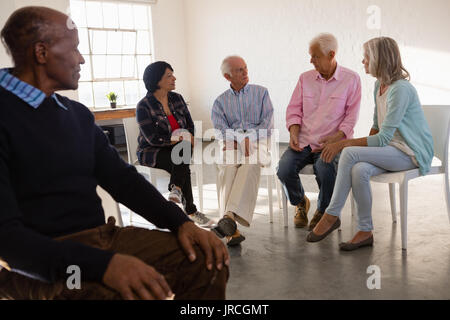 Älterer Mann an Freunden sprechen, während er auf den Vorsitz in der Kunst Klasse Stockfoto