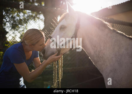 Seitenansicht der jungen Frau küssen Pferd im Stall Stockfoto