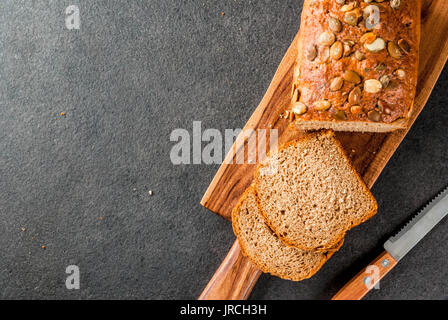 Frisch gebackene hausgemachte Bio multi Vollkornbrot mit Kürbiskernen auf einem Schneidebrett auf einem schwarzen Steintisch. Platz kopieren Stockfoto