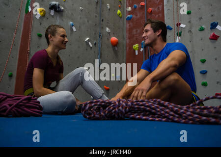 Low Angle View von Trainer Interaktion mit Athleten beim Sitzen auf dem Boden im Fitnessstudio Stockfoto