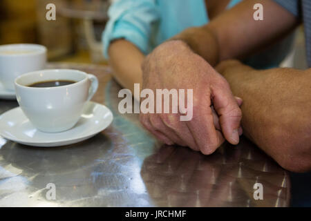 Zugeschnittenes Bild des Paares, das Hände bei Tisch im Cafe Stockfoto