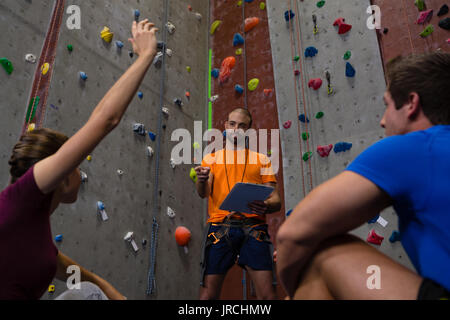 Low Angle View der männlichen Trainer Interaktion mit Athleten sitzen auf dem Boden im Fitnessstudio Stockfoto