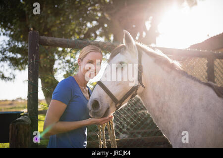 Portrait von lächelnden jungen Frau, die mit dem Pferd im Stall Stockfoto