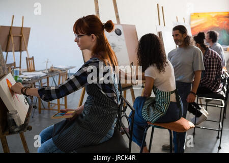 Künstler Malerei beim Sitzen auf Stuhl im Kunstunterricht Stockfoto