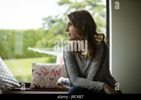 Nachdenkliche Frau auf Fensterbank zu Hause sitzen Stockfoto
