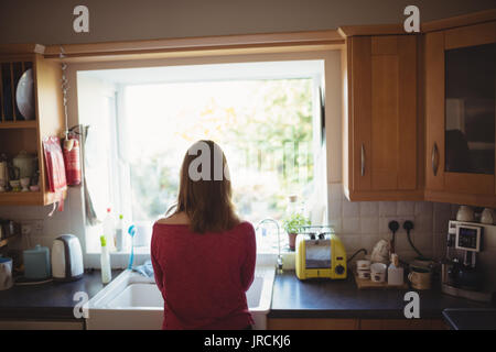 Ansicht der Rückseite des nachdenkliche Frau, die in der Küche zu Hause. Stockfoto