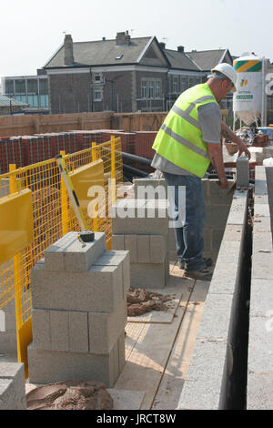Ein Maurer baut eine Mauer mit thermischen konkrete Bausteine auf einer Wohnanlage in Manchester, UK. Sicheres Arbeiten auf niedriger Ebene stahlgitterträgern. Stockfoto