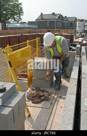Ein Maurer baut eine Mauer mit thermischen konkrete Bausteine auf einer Wohnanlage in Manchester, UK. Sicheres Arbeiten auf niedriger Ebene stahlgitterträgern. Stockfoto