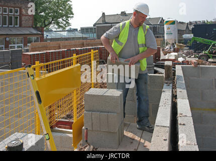 Ein Maurer baut eine Mauer mit thermischen konkrete Bausteine auf einer Wohnanlage in Manchester, UK. Sicheres Arbeiten auf niedriger Ebene stahlgitterträgern. Stockfoto