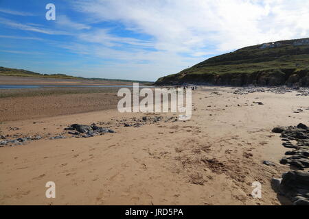 In der Ferne eine Gruppe von Hund Wanderer in die Ferne auf einem hellen sonnigen Morgen aufdem Strand verschwinden neben dem Fluss Ogmore. Stockfoto