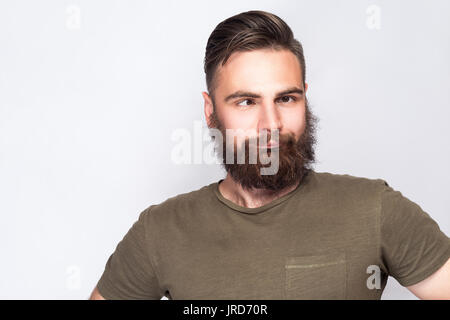 Portrait von crazy Cross eyed bärtiger Mann mit Dunkelgrünem t shirt gegen hellgrauen Hintergrund. Studio gedreht. Stockfoto