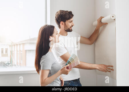 Junger Mann und Frau tun Wohnung Reparatur gemeinsam tapezieren Stockfoto