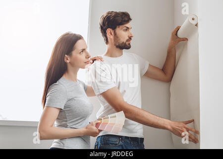 Junger Mann und Frau tun Wohnung Reparatur gemeinsam tapezieren Stockfoto