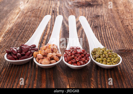 Verschiedene frische Hülsenfrüchte in Löffel auf hölzernen Tisch Stockfoto