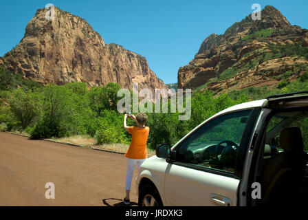 Kaukasische ältere Frau mit orangefarbenem Hemd (60-70), die mit dem Mobiltelefon im Zion National Park Springdale Utah USA fotografiert. Stockfoto