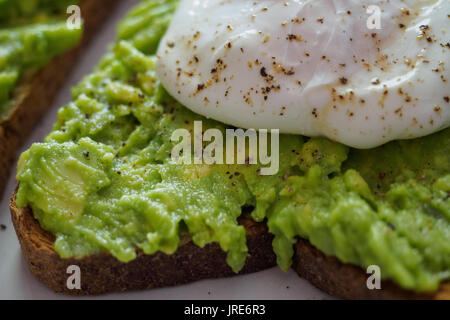 Nahaufnahme von einem pochierten Ei auf einer avocado Toast zertrümmerte mit gemahlenen schwarzen Pfeffer. Stockfoto