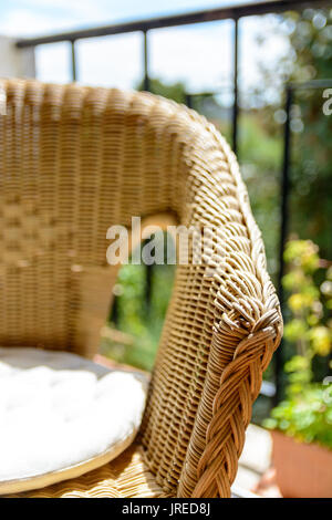 Ein rattan Stuhl mit einem weißen Kissen im Sonnenlicht auf einen Balkon mit Pflanzmaschine. Stockfoto