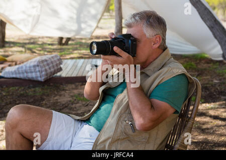 Mann fotografieren beim Sitzen auf Stuhl außerhalb Zelt Stockfoto