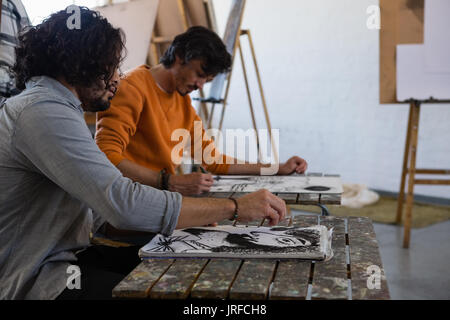 Männliche Schüler Malen auf Buch am Tisch im Kunstunterricht Stockfoto