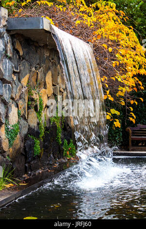 Garten Wasserfall über Sandsteinfelsen in kleine Teich mit Herbst Blätter im Hintergrund Stockfoto