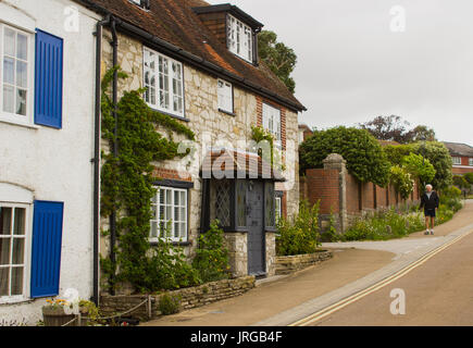 Ein einjähriger Mann geht an einem langweiligen Tag eine Straße mit malerischen Reihenhäusern in Richtung des Jachthafens im Dorf Warsash Hampshire hinunter Stockfoto