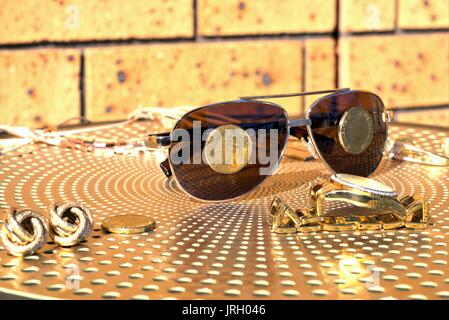 Australische Münzen auf eine Sonnenbrille. Australische 1 Dollar Münzen auf Sonnenbrillen, Gold Diamond Watch und anderen Gold Schmuck auf Tisch Stockfoto