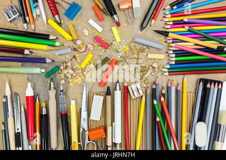 Künstler arbeiten Werkzeuge auf braun Recyclingpapier Draufsicht. Bunte Bleistifte, Pastellkreide, Spitzer, Radiergummi. Stockfoto