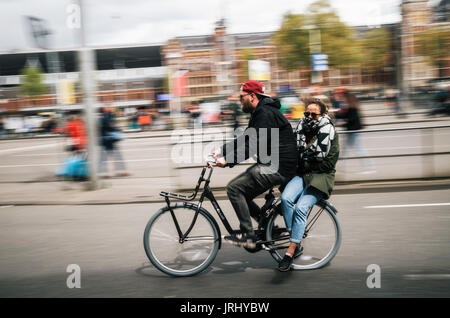 Amsterdam, Niederlande - 27 April 2017: ein Mann Radfahrer trägt eine junge Frau als Beifahrer auf dem Fahrrad, Reiten durch die Straße von Amsterdam, Niederlande Stockfoto