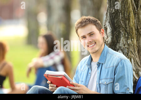 Gerne student boy Posing, sitzen Sie auf dem Gras in einem Park Stockfoto