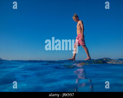 Ein gelangweilter teenaged Jungen Spaziergänge am Rande einer Infinity Pool im Urlaub Stockfoto
