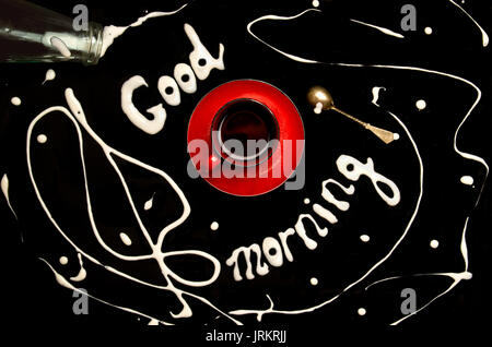 Rot Tasse Kaffee auf einem schwarzen Hintergrund und "Guten Morgen!" mit Milch geschrieben Stockfoto