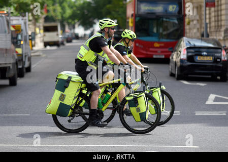 Zwei Sanitäter des NHS auf Fahrrädern, die in London mit einem roten Bus fahren. British National Health Service Medics Stockfoto