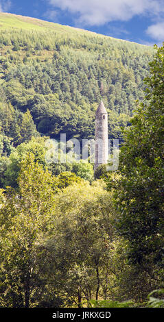 Der runde Turm der St. Kevin's Kloster Glendalough, gegen den Baum gesehen-bedeckten Berghang Stockfoto