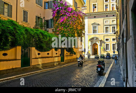 Zurück Straße in Rom mit einem bunten Bougainvillea Anlage mit rosa und orange Blumen auf der Seite eines Gebäudes mit einem Motorrad und ein Solo traveler Stockfoto