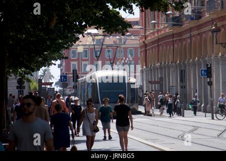 Belebte Straßenszene mit Straßenbahnen und Touristen in der Rue Gubernatis, Nizza, Frankreich Stockfoto