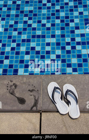 Paar blaue flip-flops und Fußabdrücke auf der Poolseite Stockfoto