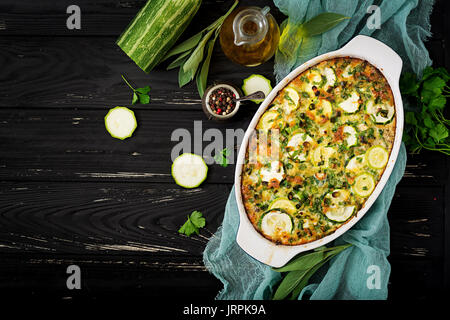 Zucchini Auflauf mit Eiern, Milch, Käse und grünen Kräutern. Flach. Ansicht von oben Stockfoto