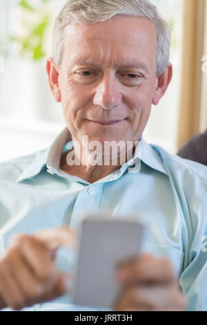 Reifer Mann zu Hause Sms auf Handy Stockfoto