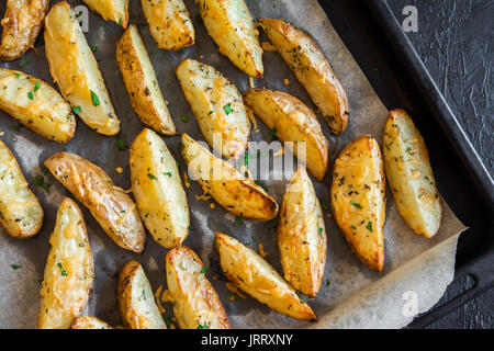 Gebackene Kartoffelecken mit Gewürzen, Käse und Kräutern auf backblech - hausgemachte Bio-gemüsegarten vegan vegetarische Snack essen. Stockfoto