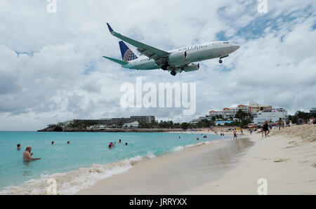 Ein United Airlines737-700 landet auf Princess Juliana International Airport als Touristen nehmen Sie Fotos von Maho Beach in Sint Maarten Stockfoto