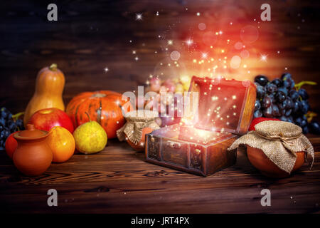 Thanksgiving-Konzept der Kürbis, Apfel, Knoblauch, Stroh und geöffneten Brust Schatz mit mystischen Wunder Licht auf Holztisch, schöne Kunst desig Stockfoto