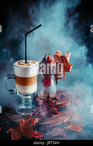 Pumpkin Spice layered Latte mit Dampf und Herbstlaub auf einem dunklen Hintergrund Stockfoto