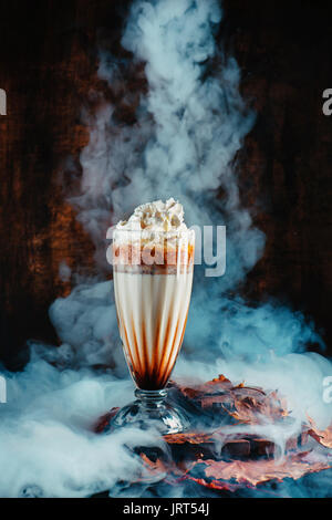 Pumpkin spice Milchshake mit Dampf und Herbstlaub auf einem dunklen Hintergrund Stockfoto
