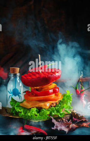 Heiße Halloween Party Burger mit Rauch und beängstigend Silhouetten in Gläsern auf einem dunklen Hintergrund Stockfoto